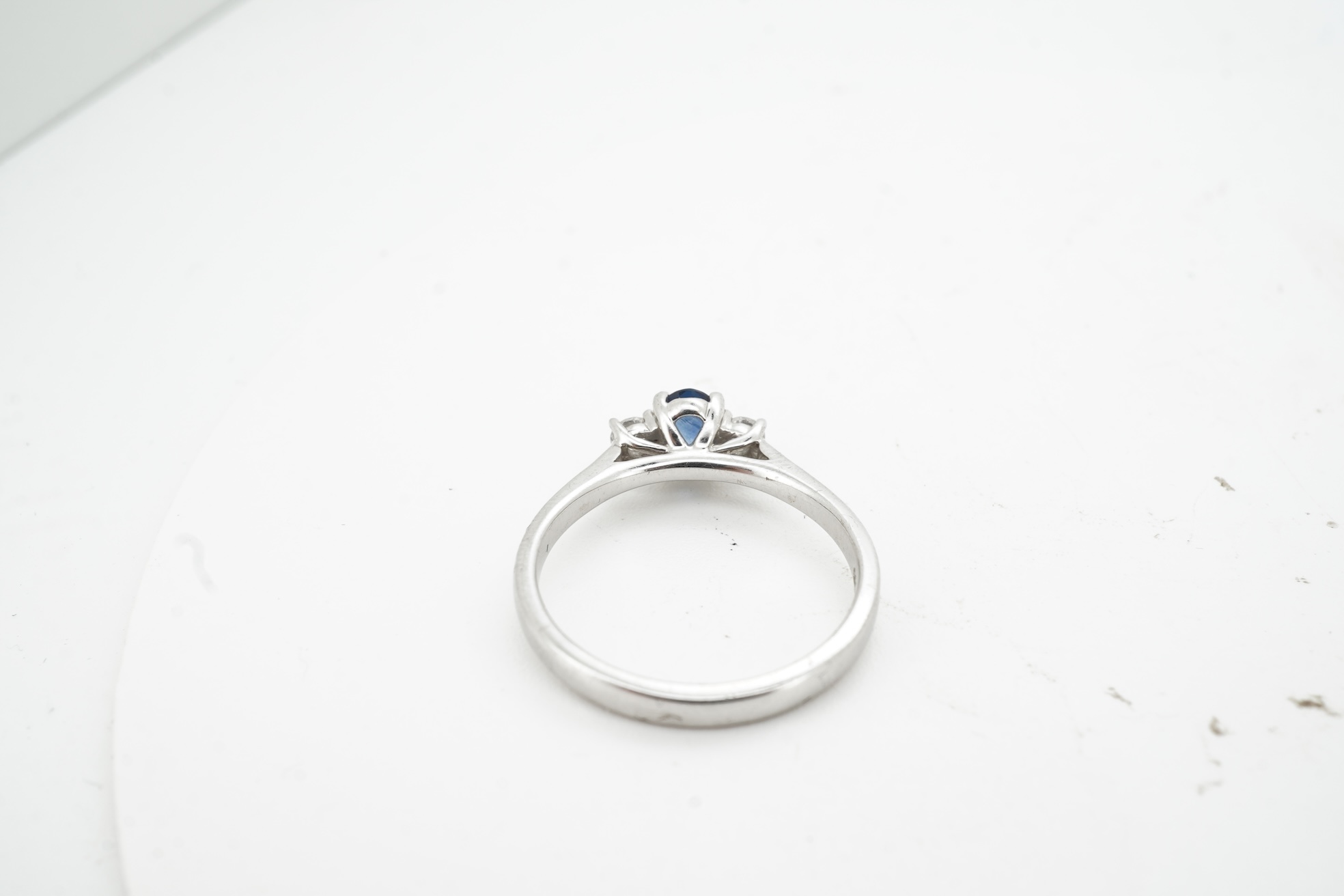 A sapphire and diamond three-stone ring, claw-set with an oval sapphire weighing approximately 0.35 carats, between shoulders set with brilliant-cut diamonds totalling approximately 0.12 carats, mounted in 9ct white gold